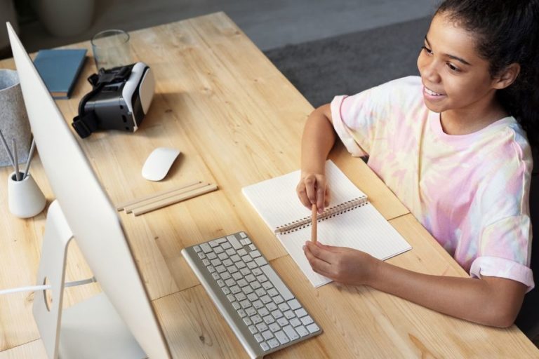 young girl sitting at a desk with pencil, paper and a computer screen. She is starting photo with eagerness.