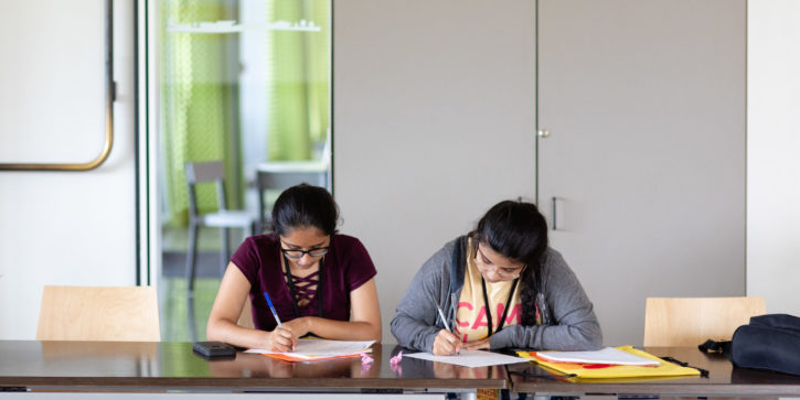 Two students sitting at table writing on paper