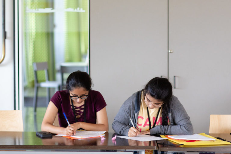 Two students sitting at table writing on paper